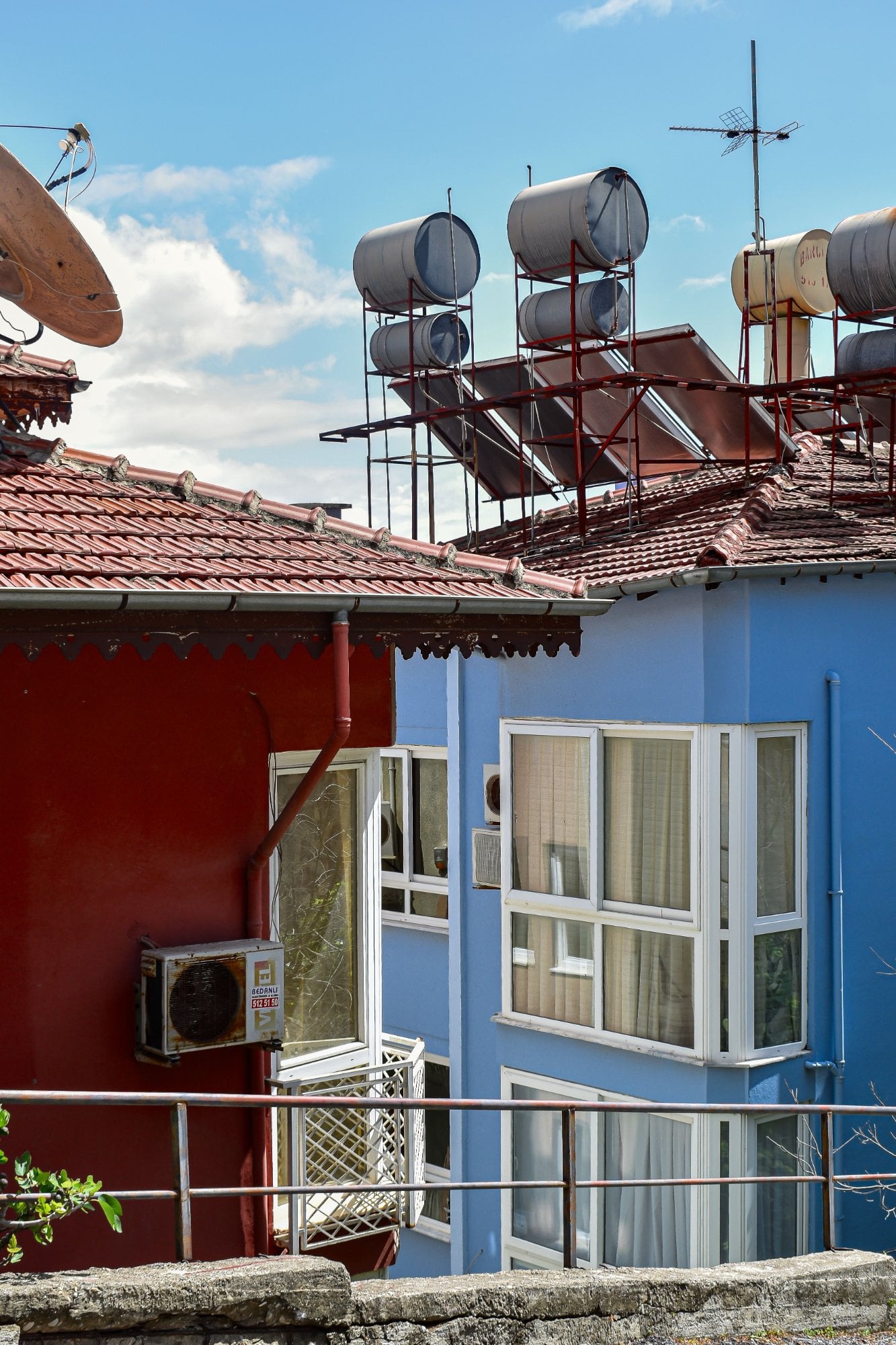 Casas roja y azul con calentadores solares y tinacos en el techo, y un aire acondicionado en la fachada